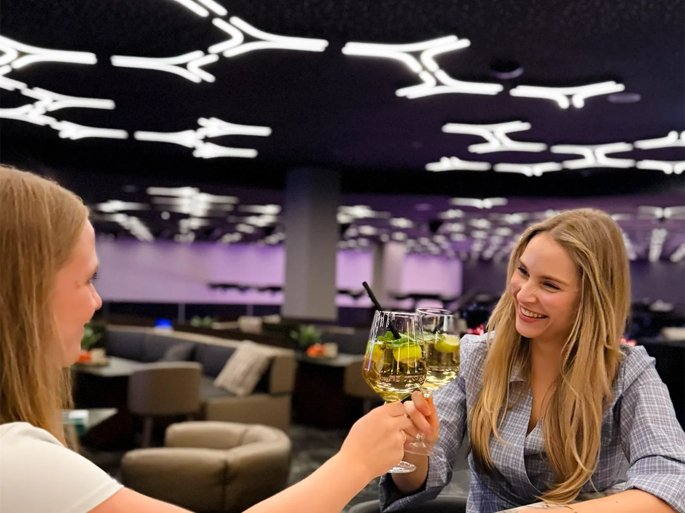 Zwei Gäste stoßen in der Lounge mit Gläsern an, darüber das beleuchtete Deckenmuster
