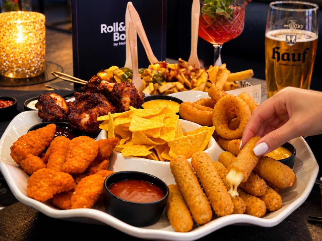Die Fingerfood-Party-Platte mit Chicken Wings, Mozzarella-Sticks, Nuggets, Nachos und Zwiebelringen, daneben ein Bier und ein Cocktail