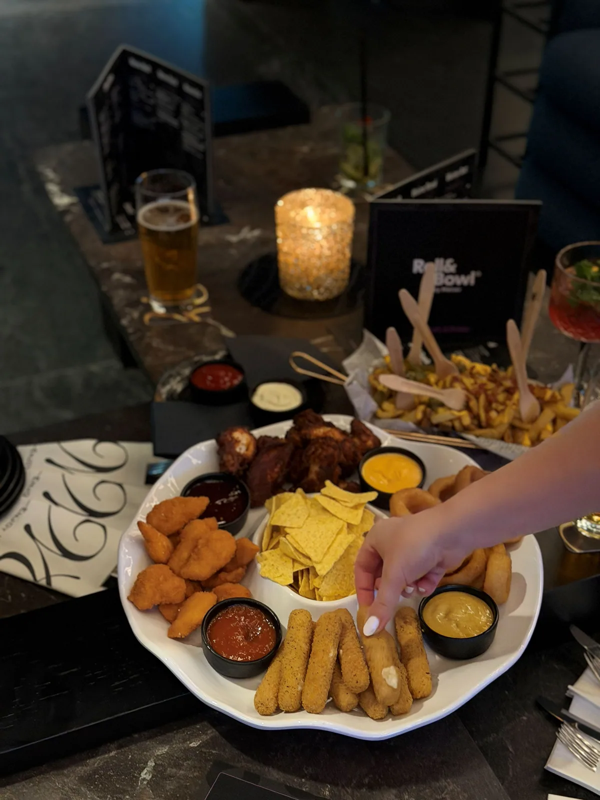 Die Fingerfood-Platte am Loungetisch, daneben Käse-Pommes, Bier und ein Cocktail