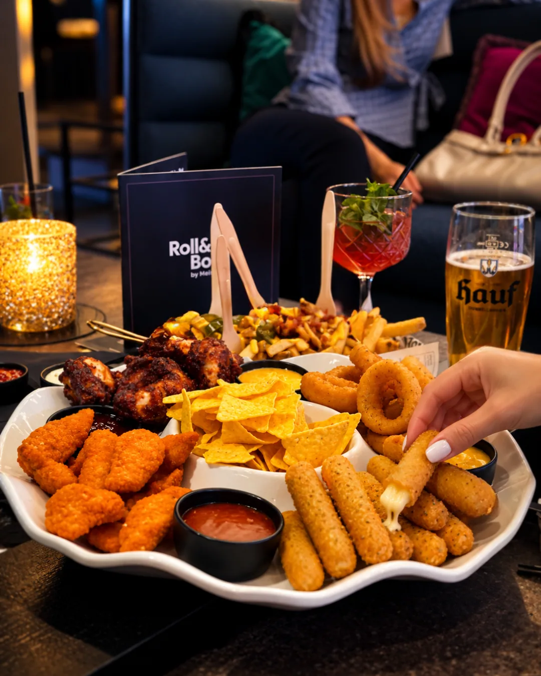 Die Fingerfood-Platte mit Mozzarella Sticks, Nuggets, Chicken Wings, Nachos und Dips, daneben ein Hauf Bier und ein Cocktail